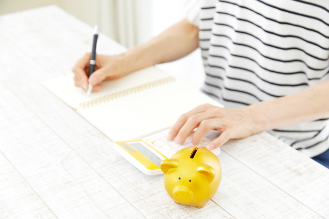 家計簿をつけている女性と豚の貯金箱